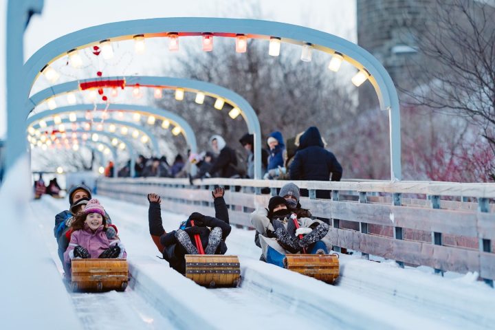 People sledding on a snow track with overhead lights and snowy surroundings.