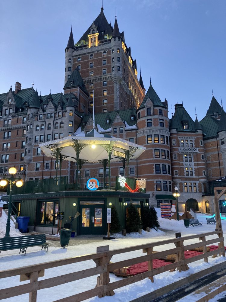 Historic building with green roofs, snow, and a lit structure in the foreground.
