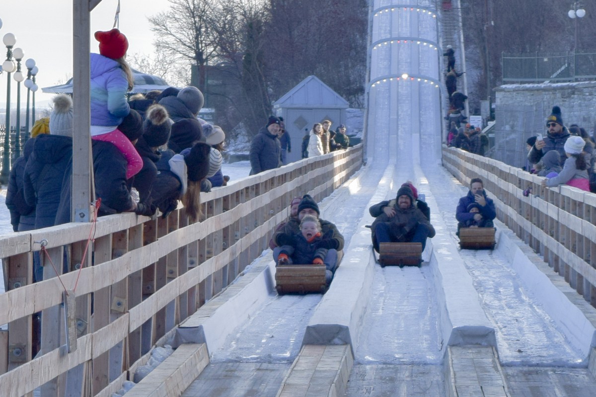 People sledding down an ice slide with onlookers watching on a snowy day.