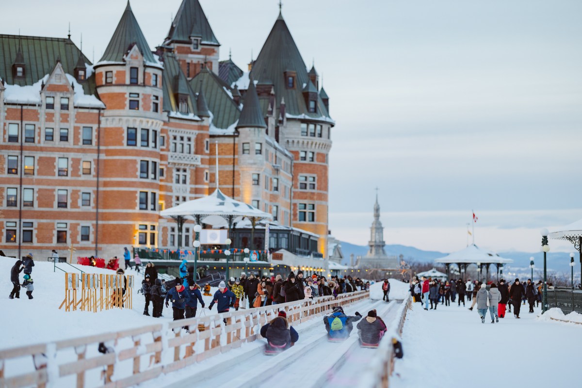 People sledding on a snowy track near a large castle-like building.