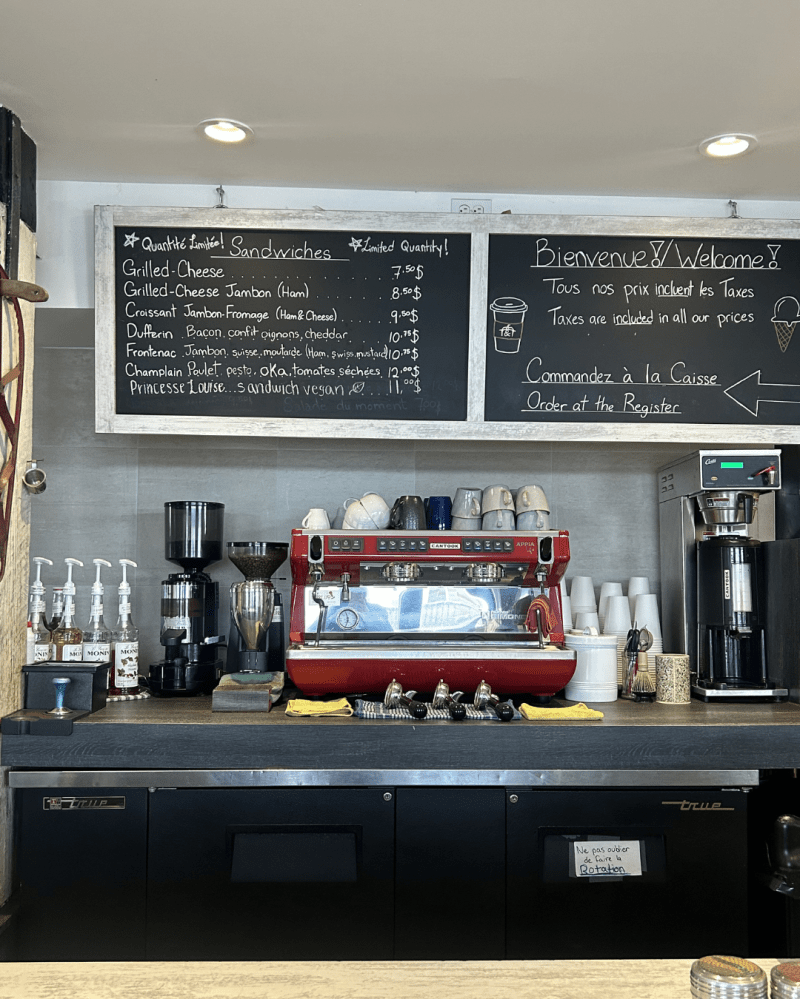 Cafe counter with espresso machine, coffee pots, and sandwich menu on chalkboard.