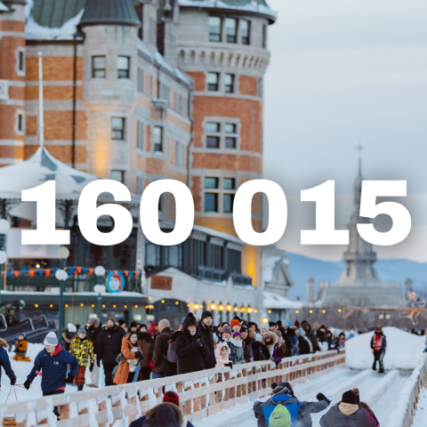People sledding down a snowy track with a large building in the background.