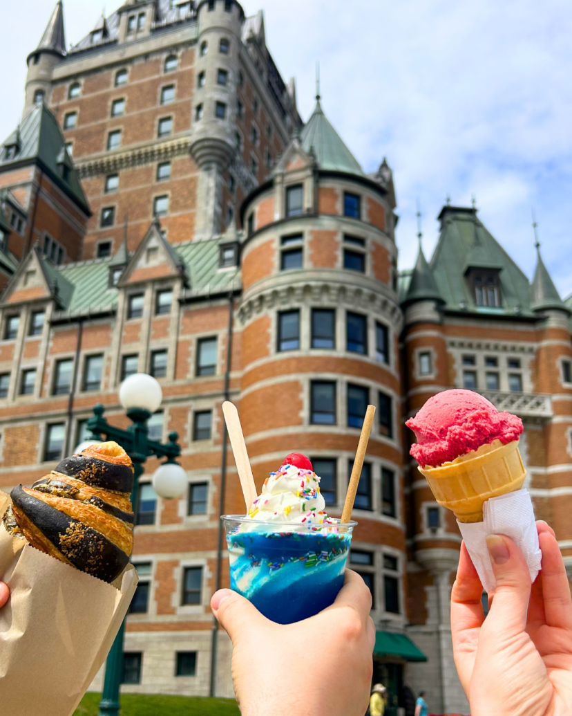 Hands holding pastries and ice cream in front of a castle-like building.