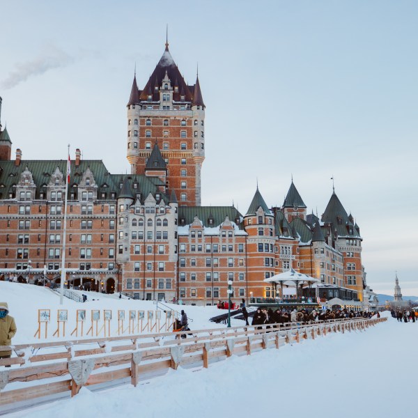 Snow-covered Château Frontenac with boardwalk and people in winter.