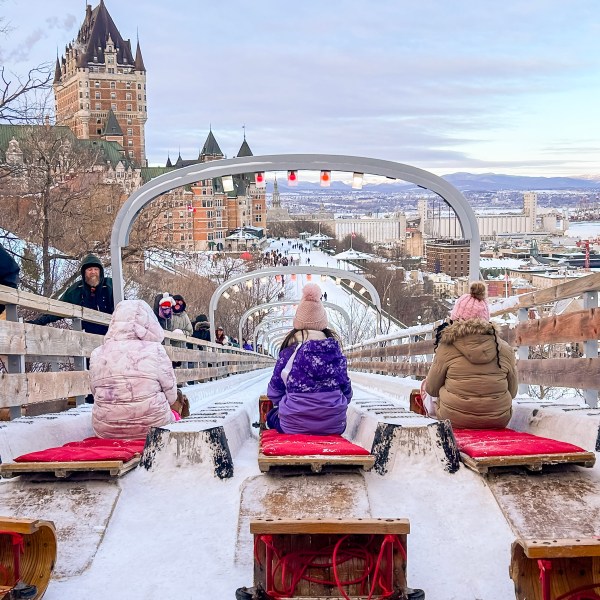 Four people on sleds ready to slide down an icy track in a snowy cityscape.