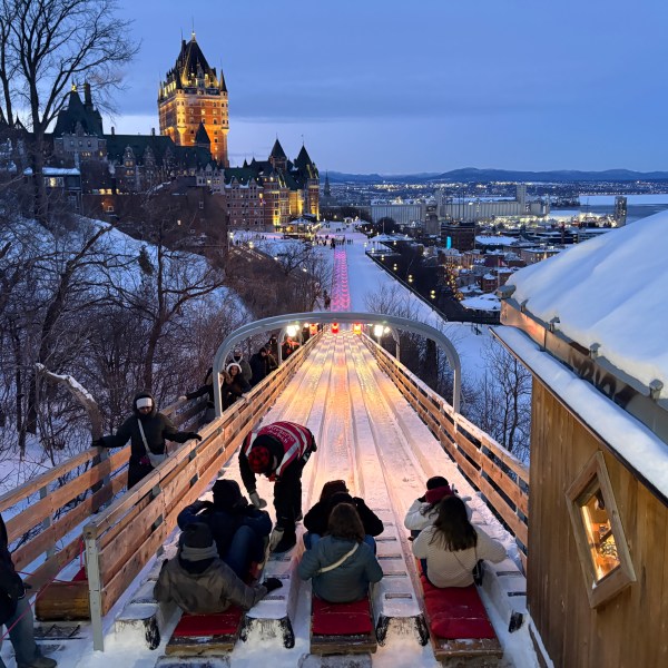People sledding on a wooden slide with a historic building in the background at dusk.