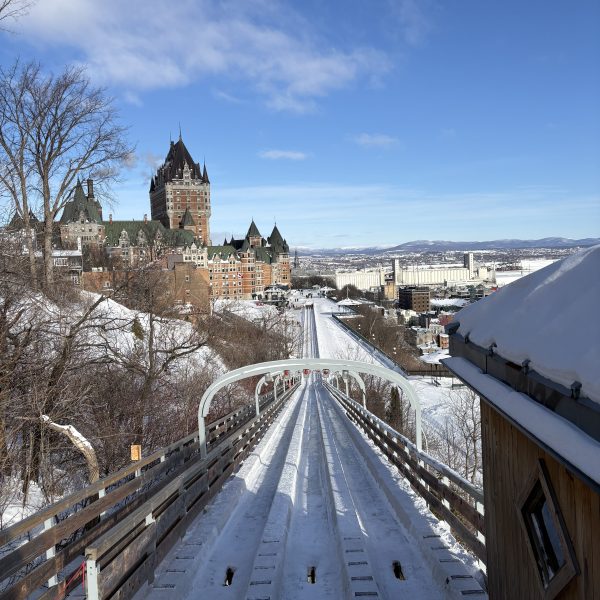Snowy cityscape with a toboggan slide view, large historic building, and blue sky.